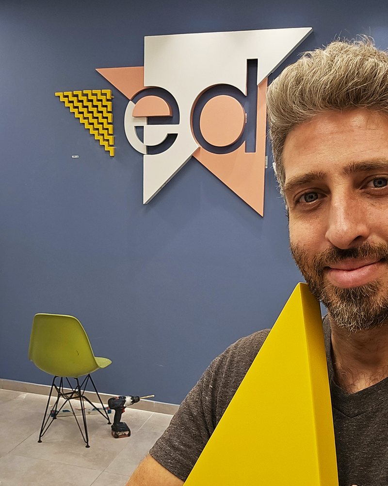 עידן הרבט ליד הלוגו המותקן בכניסה למשרד